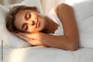 Beautiful young woman sleeping while lying in bed comfortably and blissfully. Sunbeam dawn  on her face